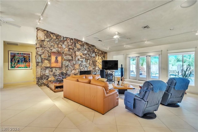 tiled living room featuring ceiling fan, a stone fireplace, rail lighting, and french doors