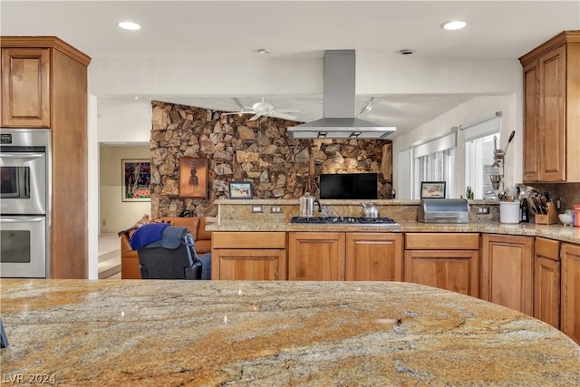 kitchen featuring ceiling fan, island range hood, light stone counters, and stainless steel appliances