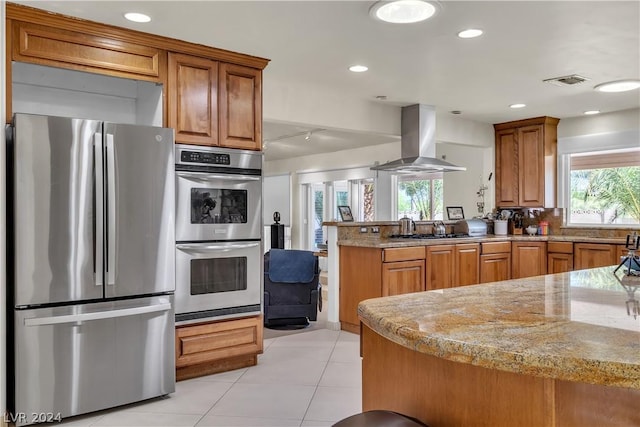 kitchen with kitchen peninsula, light stone counters, a wealth of natural light, stainless steel appliances, and exhaust hood