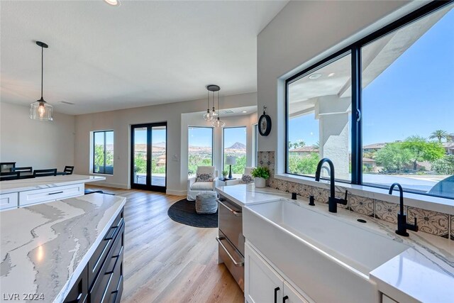 kitchen featuring light hardwood / wood-style flooring, white cabinets, light stone counters, decorative light fixtures, and sink