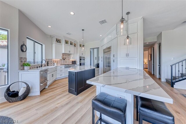 kitchen with white cabinetry, a kitchen island, appliances with stainless steel finishes, backsplash, and pendant lighting