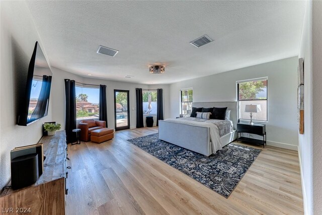 bedroom with a textured ceiling, multiple windows, and light hardwood / wood-style flooring