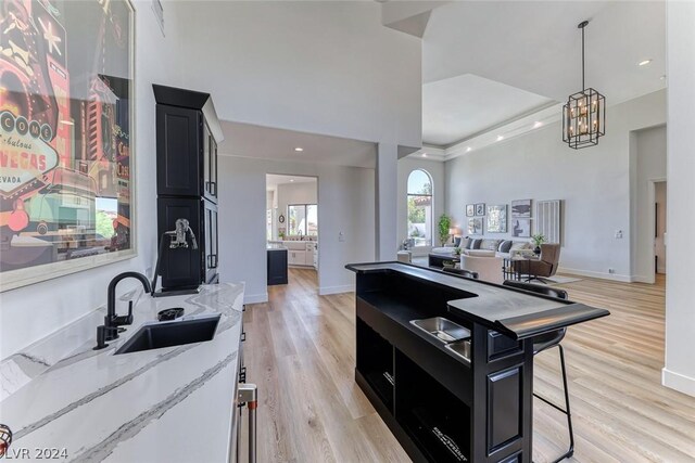 kitchen featuring decorative light fixtures, light hardwood / wood-style floors, a notable chandelier, light stone countertops, and sink