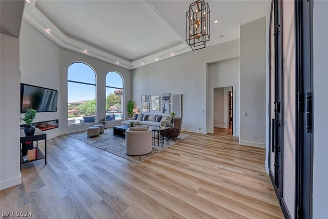 living room featuring a high ceiling, light wood-type flooring, a raised ceiling, and an inviting chandelier