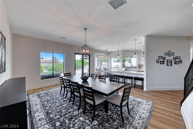 dining area featuring a textured ceiling, light wood-type flooring, a wealth of natural light, and a chandelier