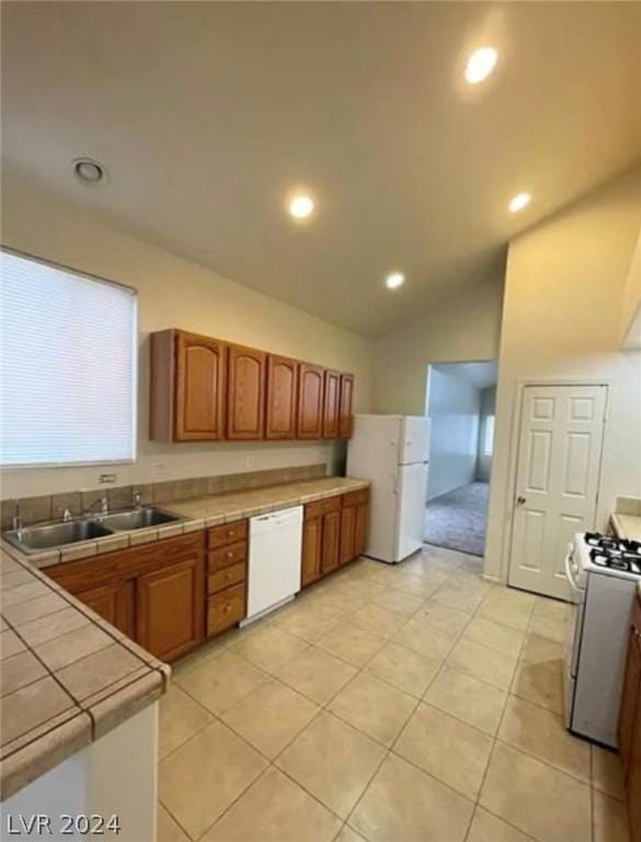 kitchen featuring white appliances, tile counters, sink, vaulted ceiling, and light tile patterned floors