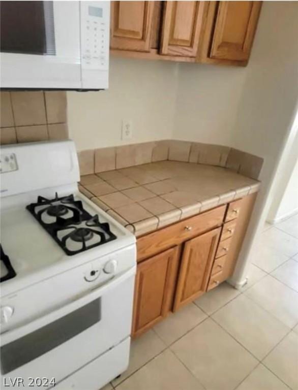 kitchen with tile counters, light tile patterned floors, and white appliances