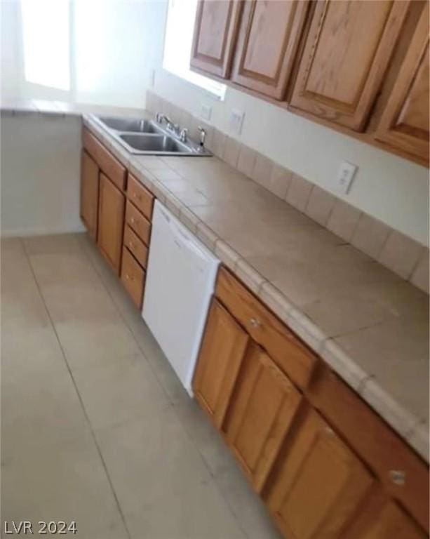 kitchen with light tile patterned flooring, tile counters, white dishwasher, and sink