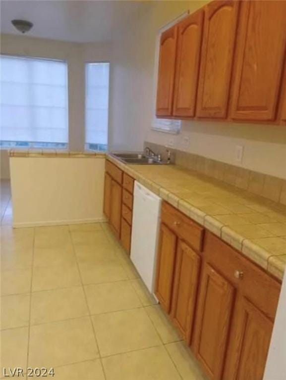 kitchen with sink, kitchen peninsula, tile countertops, light tile patterned flooring, and white dishwasher