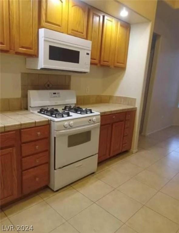 kitchen featuring light tile patterned floors, tile counters, and white appliances