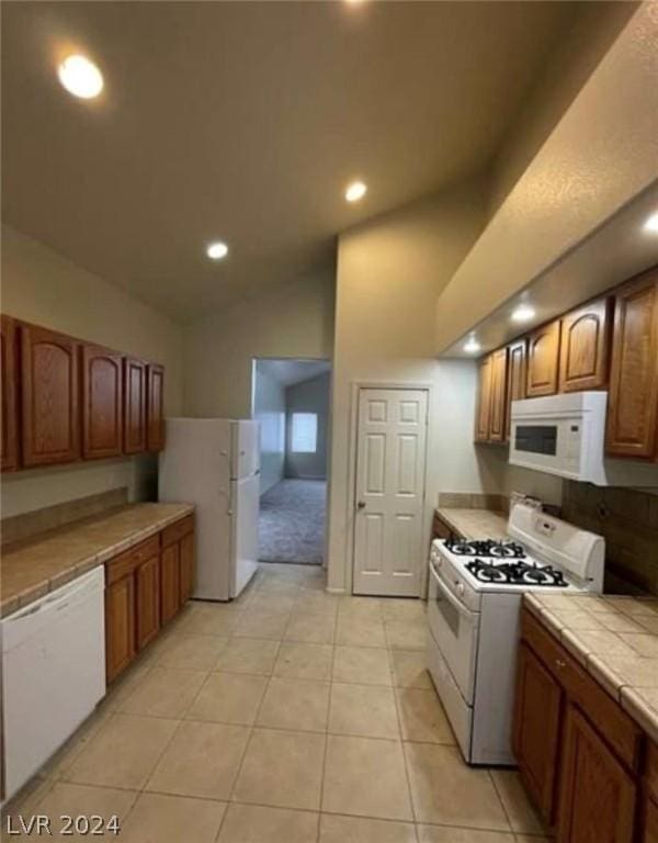 kitchen with light tile patterned flooring, white appliances, tile counters, and vaulted ceiling