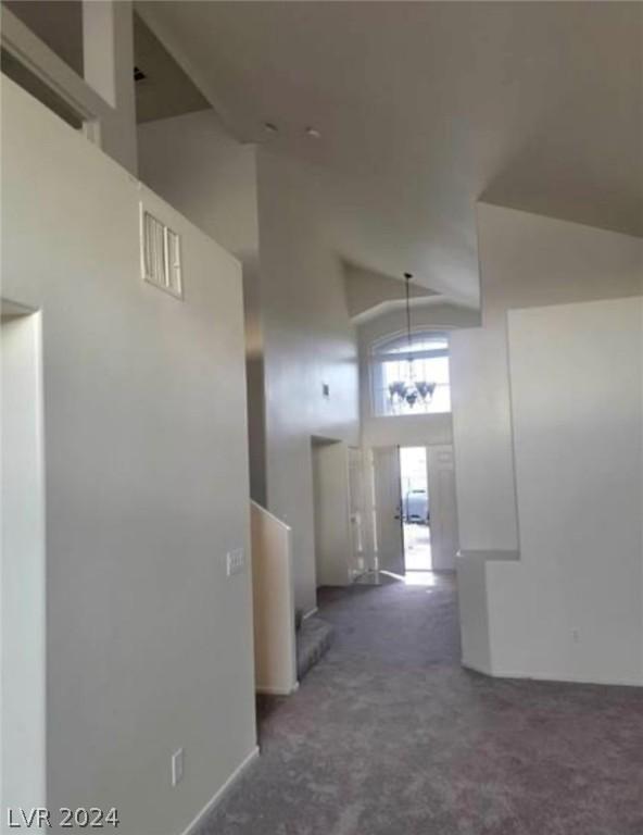 corridor featuring high vaulted ceiling, a notable chandelier, and dark colored carpet