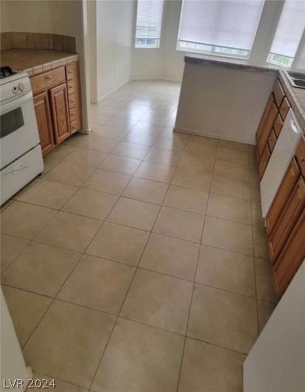 kitchen with light tile patterned floors, white range with gas stovetop, and tile countertops