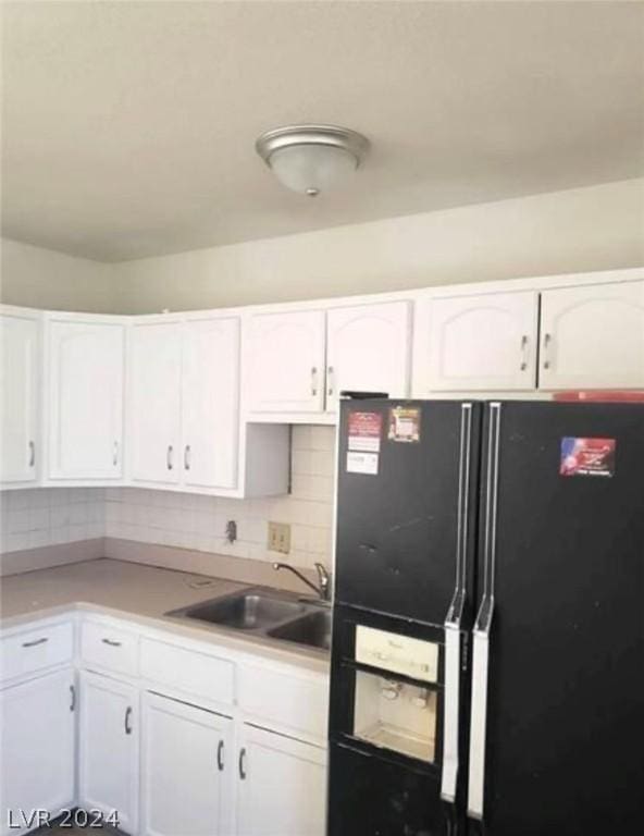 kitchen with black fridge, white cabinetry, backsplash, and sink