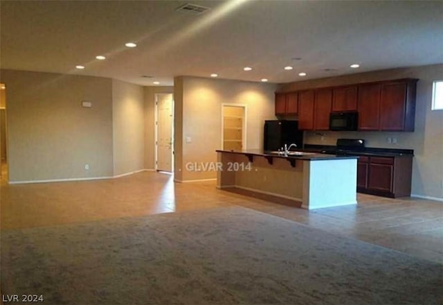 kitchen with sink, a kitchen breakfast bar, black appliances, a center island with sink, and light carpet