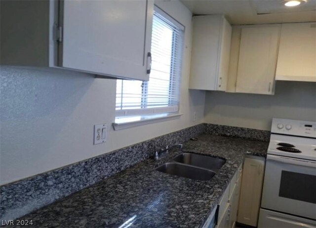 kitchen featuring white range with electric cooktop, sink, white cabinets, and dark stone counters