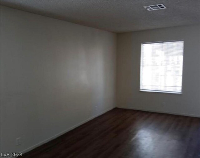 empty room with a textured ceiling and dark hardwood / wood-style flooring