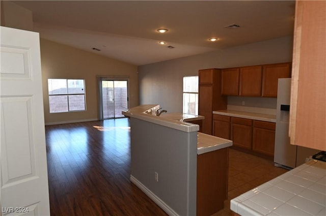 kitchen featuring vaulted ceiling, tile countertops, dark hardwood / wood-style flooring, a center island, and white fridge with ice dispenser