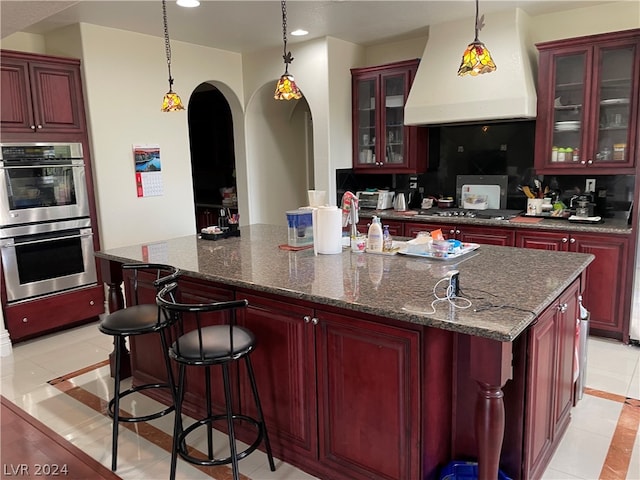 kitchen with appliances with stainless steel finishes, light tile floors, custom range hood, and pendant lighting