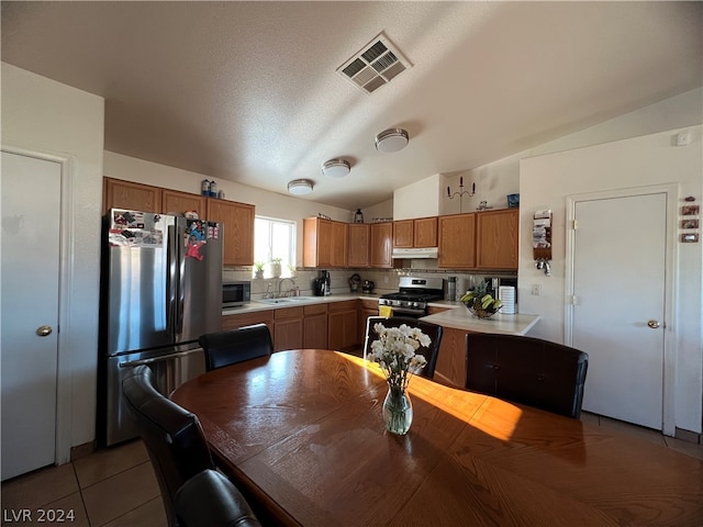 kitchen featuring lofted ceiling, tasteful backsplash, light tile patterned floors, appliances with stainless steel finishes, and sink