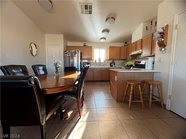 kitchen featuring decorative backsplash, sink, stove, stainless steel fridge, and light tile patterned floors