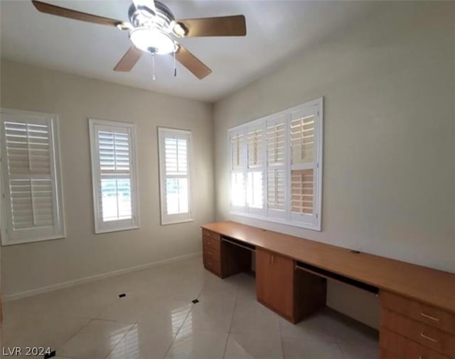 unfurnished office with built in desk, ceiling fan, and light tile patterned flooring