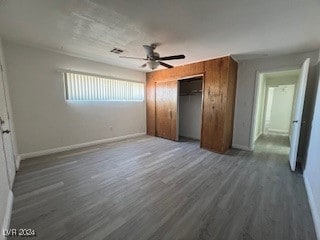 unfurnished bedroom with a closet, dark hardwood / wood-style floors, ceiling fan, and wood walls