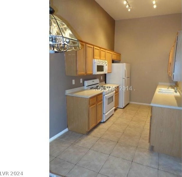 kitchen with a towering ceiling, white appliances, track lighting, light tile floors, and sink