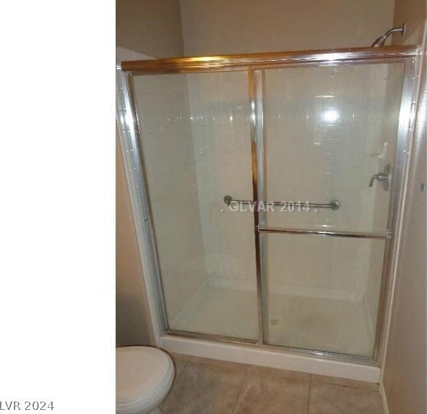 bathroom featuring tile floors, a shower with door, and toilet