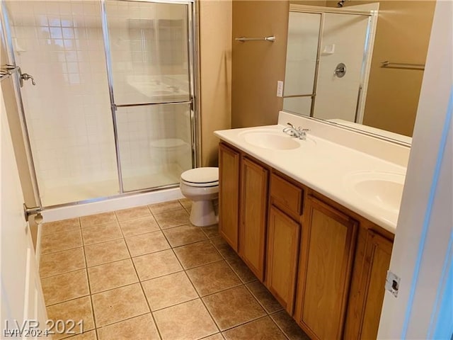 bathroom featuring a shower with door, double sink vanity, tile flooring, and toilet