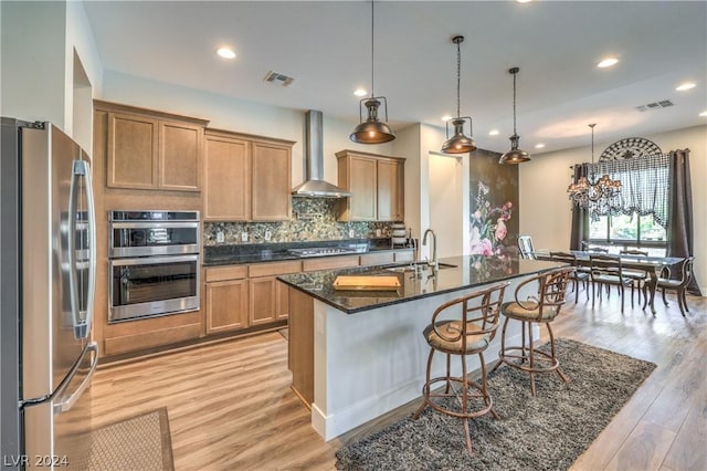 kitchen featuring decorative light fixtures, sink, stainless steel appliances, wall chimney range hood, and light hardwood / wood-style flooring