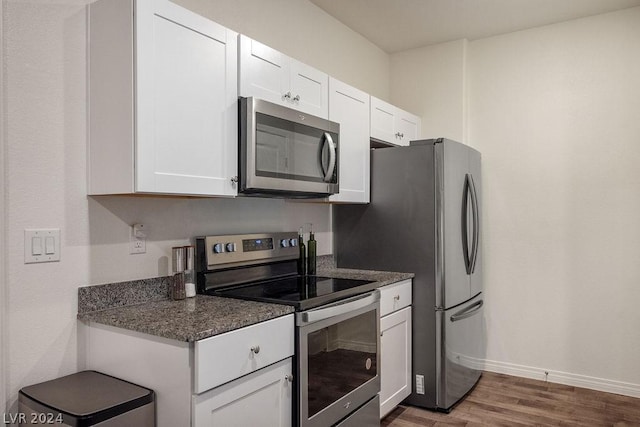 kitchen with white cabinetry, appliances with stainless steel finishes, dark hardwood / wood-style floors, and dark stone counters