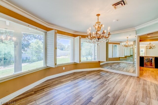 unfurnished dining area with light hardwood / wood-style floors, a chandelier, ornamental molding, and beverage cooler