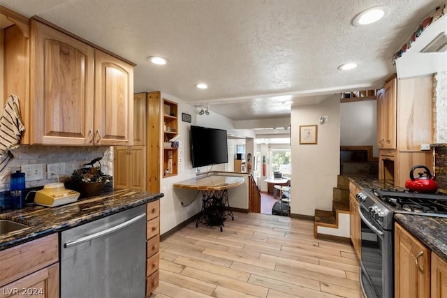 kitchen featuring tasteful backsplash, range with gas stovetop, dark stone counters, stainless steel dishwasher, and light hardwood / wood-style floors