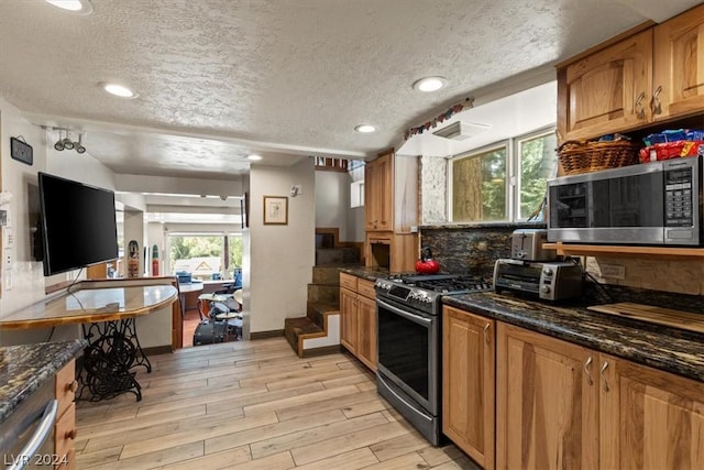 kitchen featuring light hardwood / wood-style floors, stainless steel appliances, a textured ceiling, and dark stone countertops