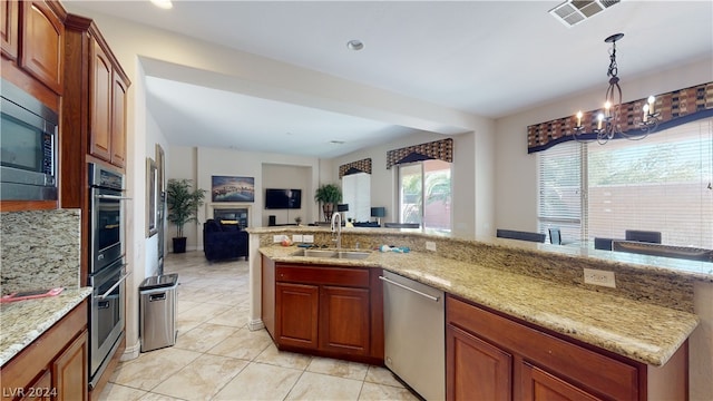 kitchen with stainless steel appliances, light stone countertops, sink, and decorative light fixtures