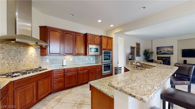 kitchen with sink, a kitchen breakfast bar, stainless steel appliances, a kitchen island with sink, and wall chimney range hood