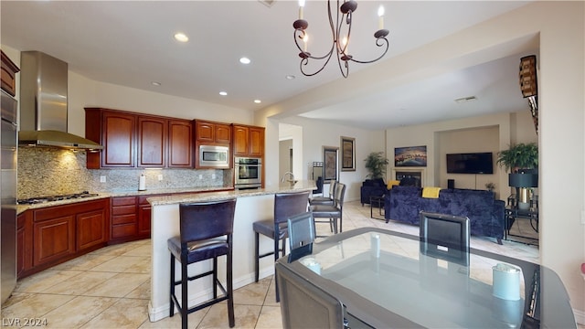 kitchen with appliances with stainless steel finishes, decorative light fixtures, a kitchen breakfast bar, decorative backsplash, and wall chimney exhaust hood