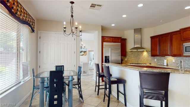 kitchen featuring built in appliances, light stone counters, a wealth of natural light, decorative backsplash, and wall chimney exhaust hood