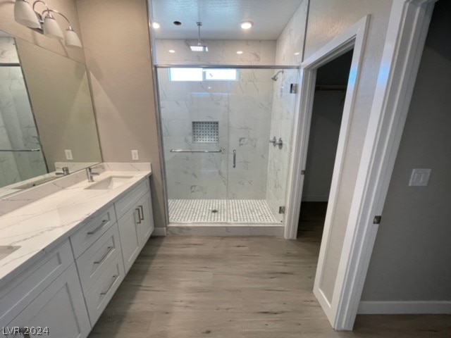 bathroom with a shower with shower door, hardwood / wood-style floors, and dual bowl vanity