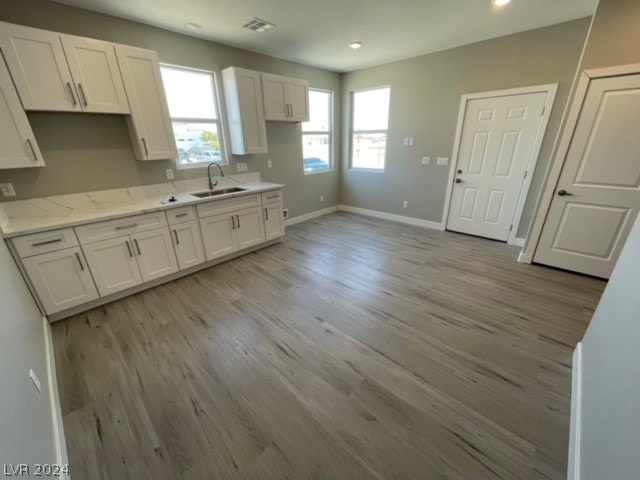 kitchen featuring sink, white cabinetry, light stone countertops, and hardwood / wood-style floors