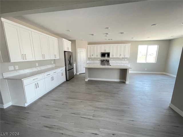 kitchen with appliances with stainless steel finishes, light hardwood / wood-style flooring, and a kitchen island with sink