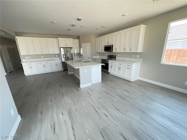 kitchen with light hardwood / wood-style floors, appliances with stainless steel finishes, white cabinetry, and a kitchen island with sink