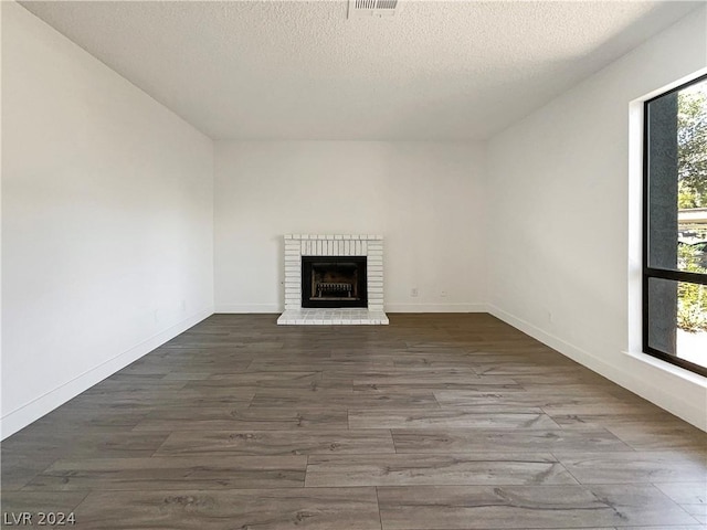 unfurnished living room featuring a textured ceiling, dark wood-type flooring, plenty of natural light, and a fireplace