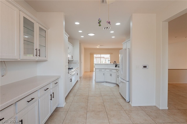 kitchen featuring light tile patterned floors, white fridge, white cabinetry, and sink