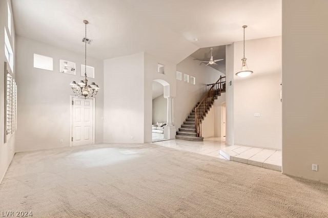 unfurnished living room with ceiling fan with notable chandelier, high vaulted ceiling, and light carpet