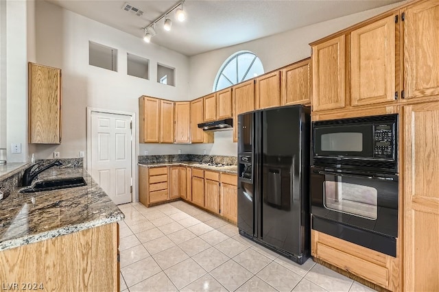 kitchen with sink, light tile patterned floors, light stone counters, and black appliances