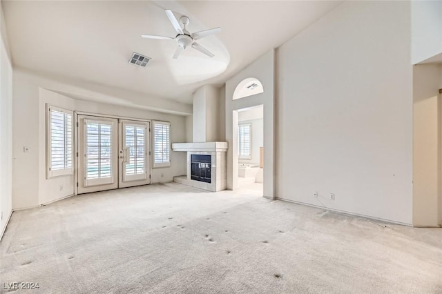 unfurnished living room with ceiling fan, light colored carpet, a tile fireplace, and french doors