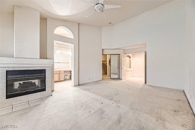 unfurnished living room with ceiling fan, light colored carpet, a tiled fireplace, and a towering ceiling