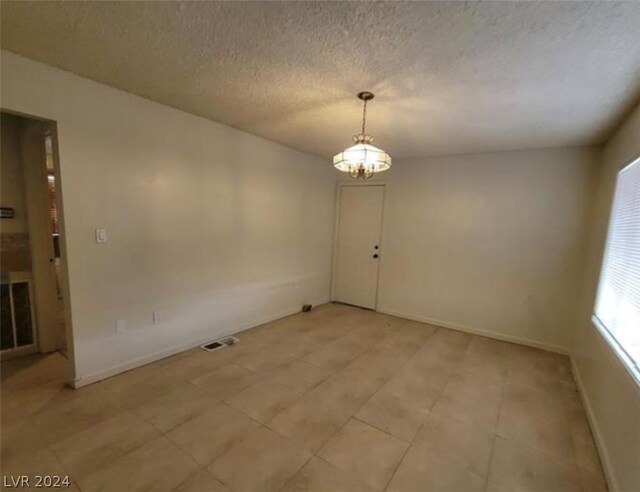 spare room with a chandelier, tile flooring, and a textured ceiling